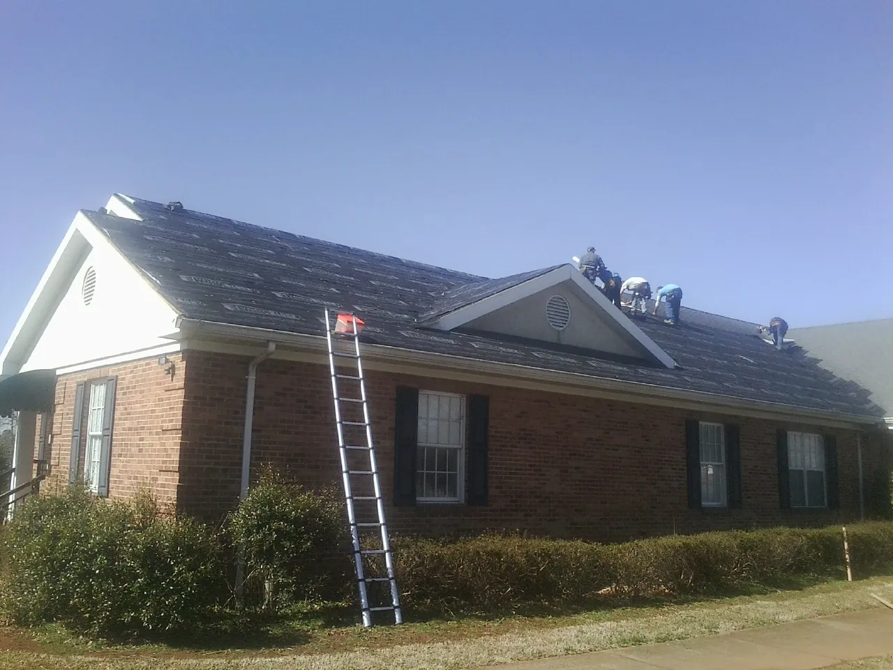 Crew tearing shingles off a brick ranch roof with a ladder set — Emergency Roof Repair work by our crew in Malta