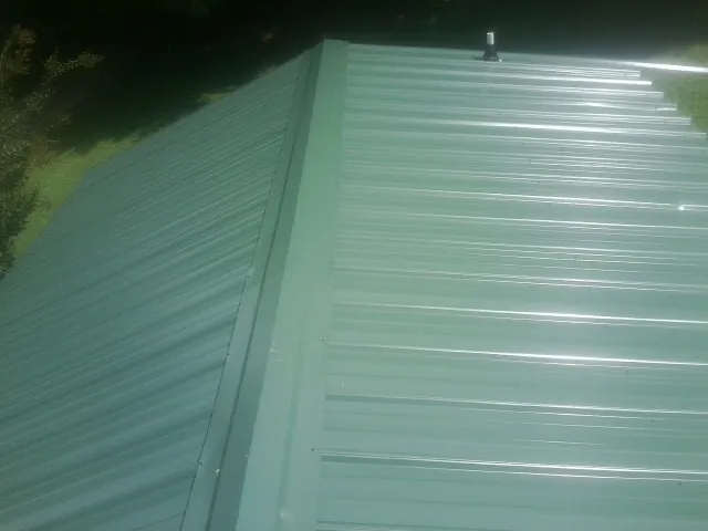 New green metal panels meeting at the ridge of a roof — Flat Roof Repair work by our crew in Malta